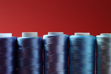 Photo of Spools of colorful sewing threads on red background, closeup