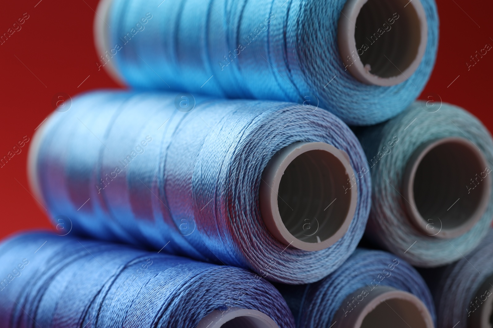 Photo of Spools of colorful sewing threads on red background, closeup