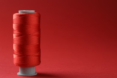 Photo of Spool of colorful sewing thread on red background, space for text