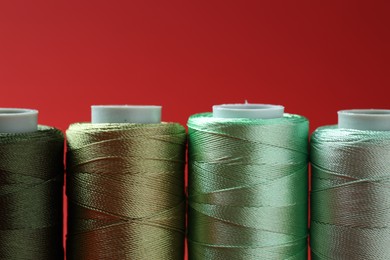 Photo of Spools of colorful sewing threads on red background, closeup