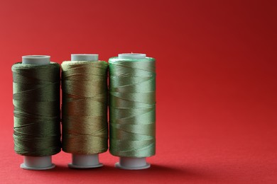 Photo of Spools of colorful sewing threads on red background, space for text