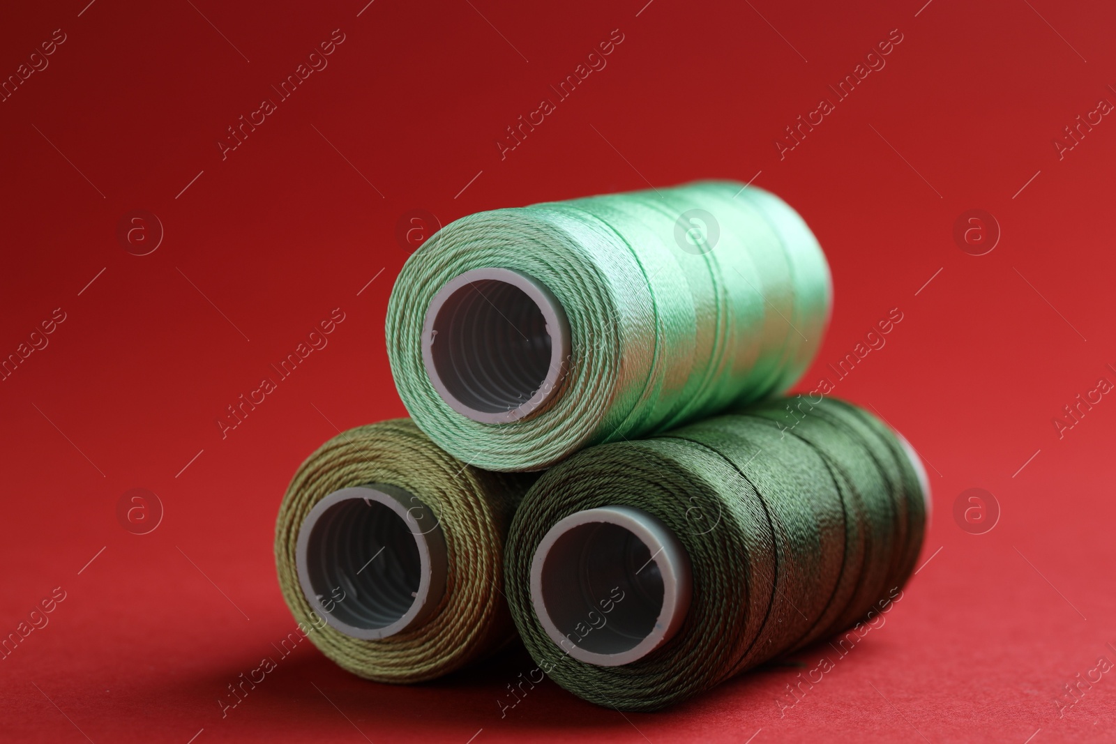 Photo of Spools of colorful sewing threads on red background, closeup