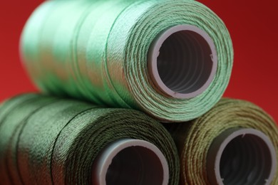 Photo of Spools of colorful sewing threads on red background, closeup