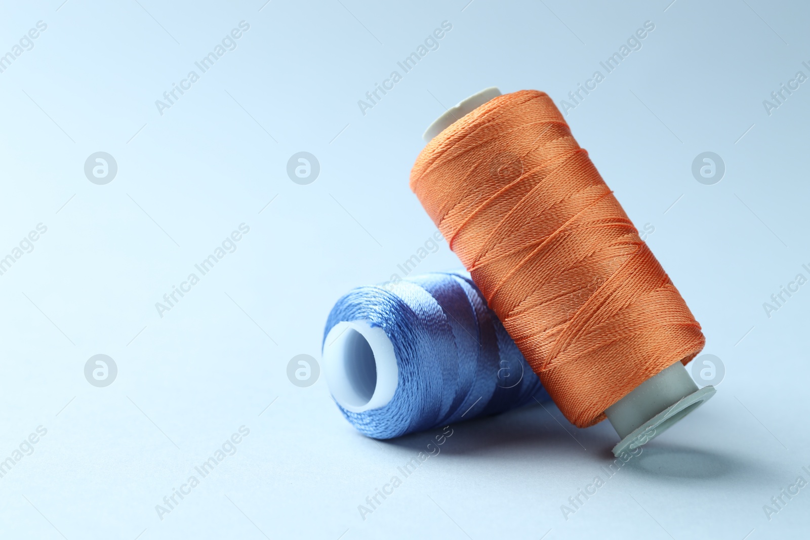 Photo of Spools of colorful sewing threads on light background, space for text