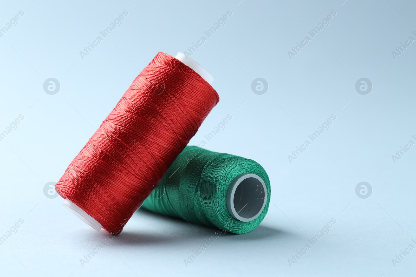 Photo of Spools of colorful sewing threads on light background, space for text