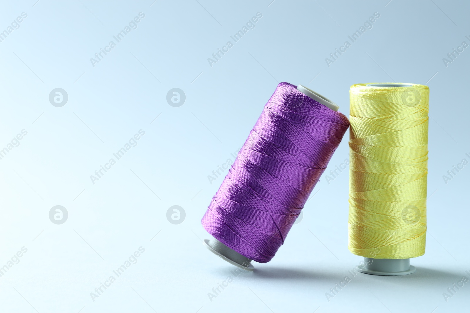 Photo of Spools of colorful sewing threads on light background, space for text