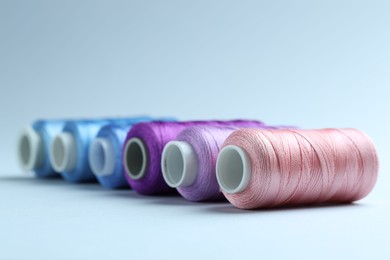 Photo of Spools of colorful sewing threads on light background, closeup