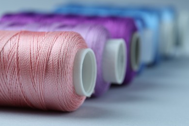 Photo of Spools of colorful sewing threads on light background, closeup. Space for text