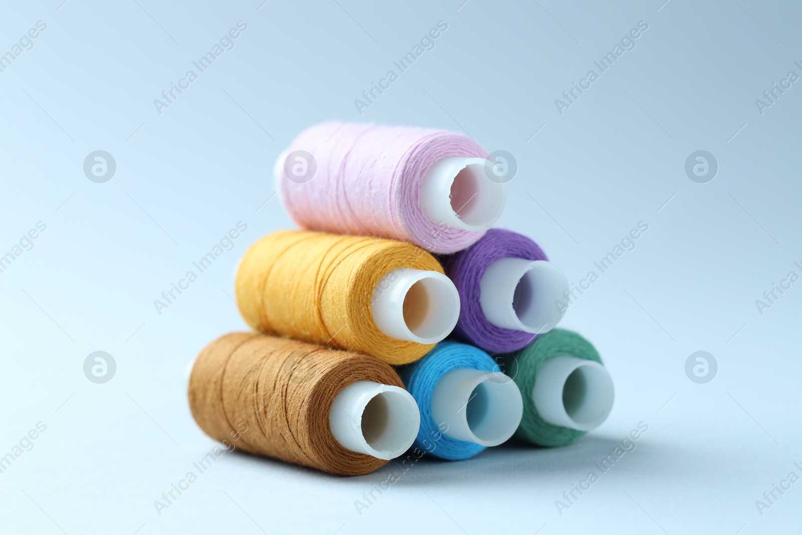 Photo of Spools of colorful sewing threads on light background, closeup