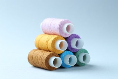 Photo of Spools of colorful sewing threads on light background, closeup