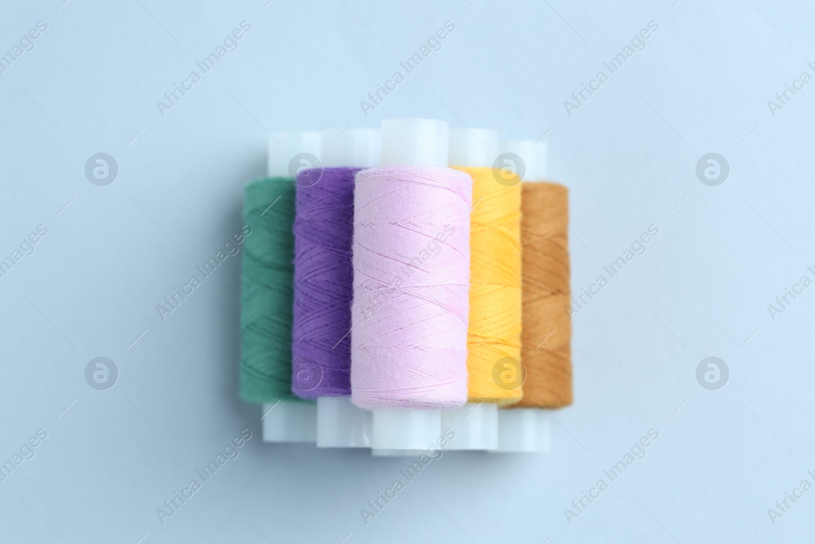 Photo of Spools of colorful sewing threads on light background, top view