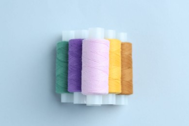 Photo of Spools of colorful sewing threads on light background, top view