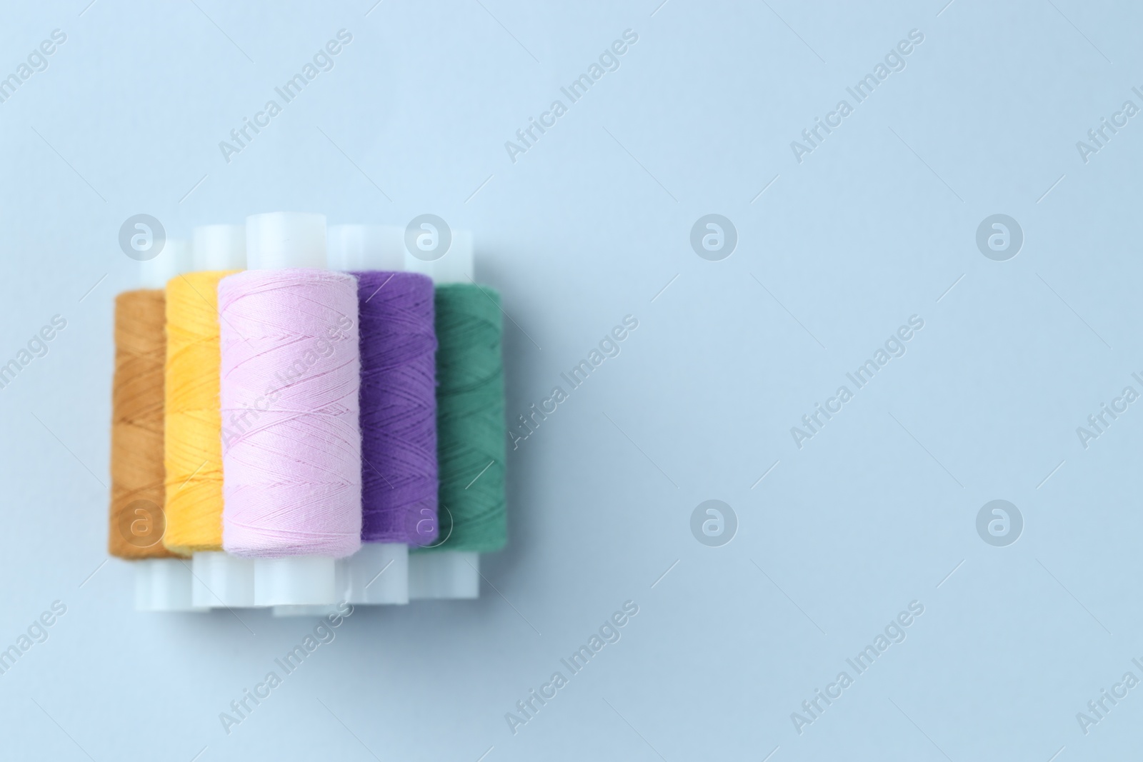 Photo of Spools of colorful sewing threads on light background, top view. Space for text