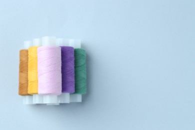 Photo of Spools of colorful sewing threads on light background, top view. Space for text