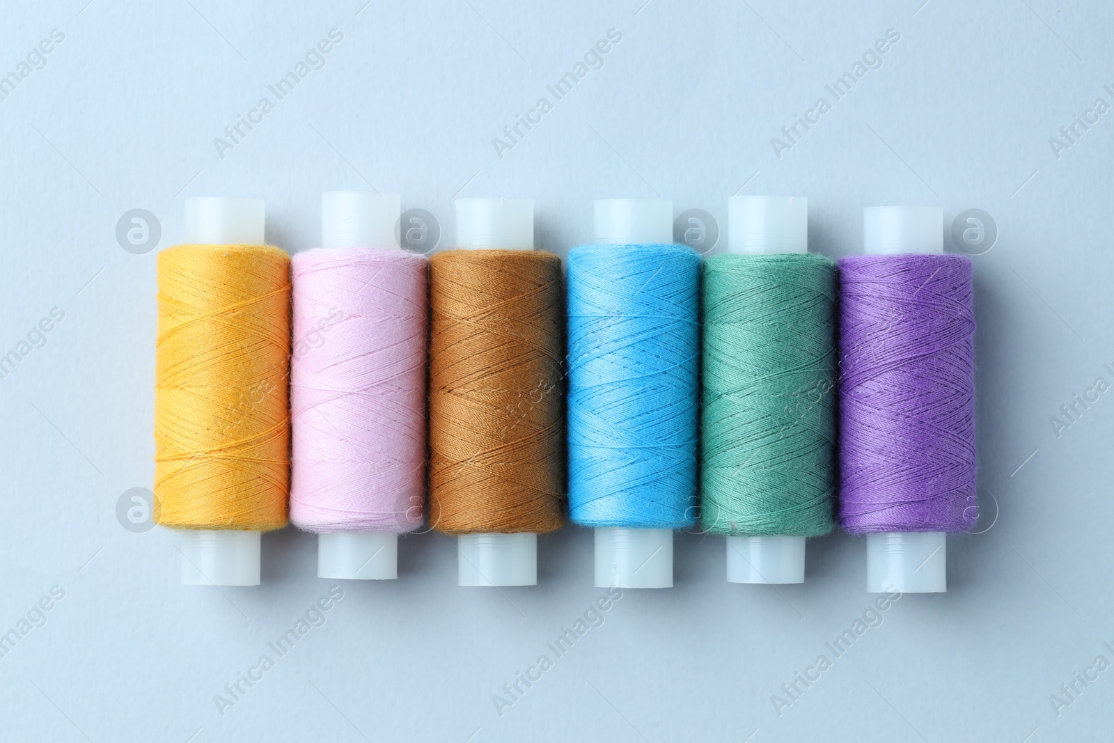 Photo of Spools of colorful sewing threads on light background, flat lay