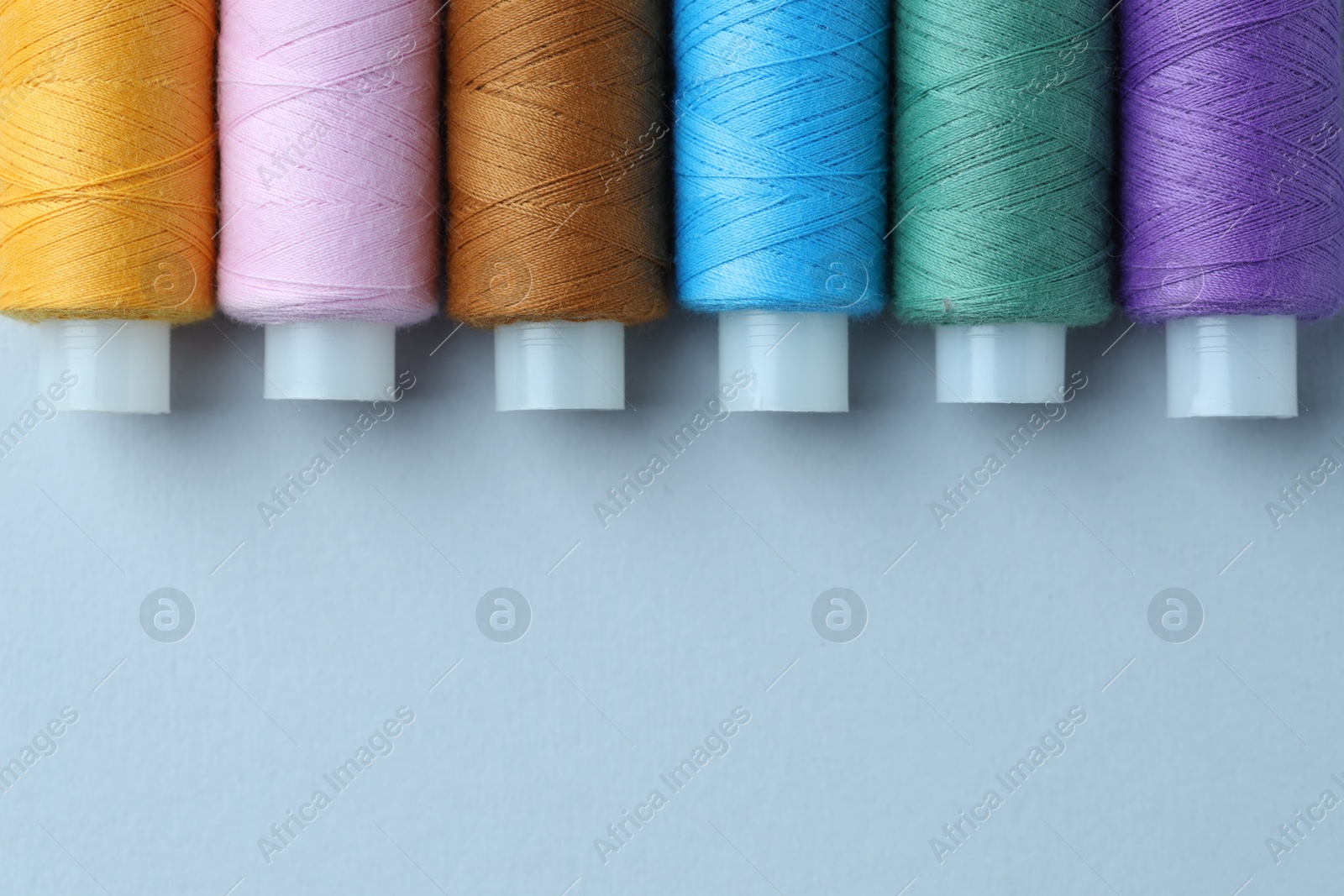 Photo of Spools of colorful sewing threads on light background, flat lay. Space for text