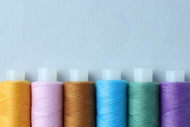 Photo of Spools of colorful sewing threads on light background, flat lay. Space for text