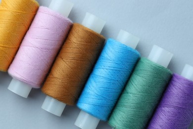 Photo of Spools of colorful sewing threads on light background, flat lay