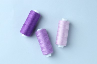 Photo of Spools of colorful sewing threads on light background, flat lay