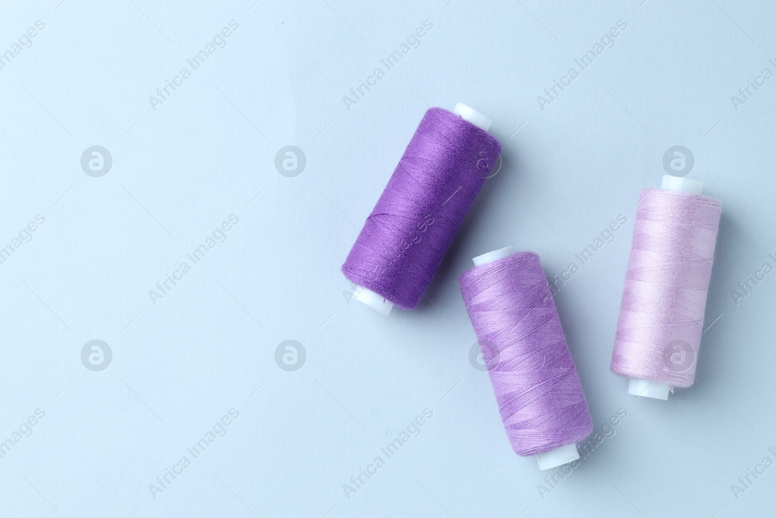 Photo of Spools of colorful sewing threads on light background, flat lay. Space for text