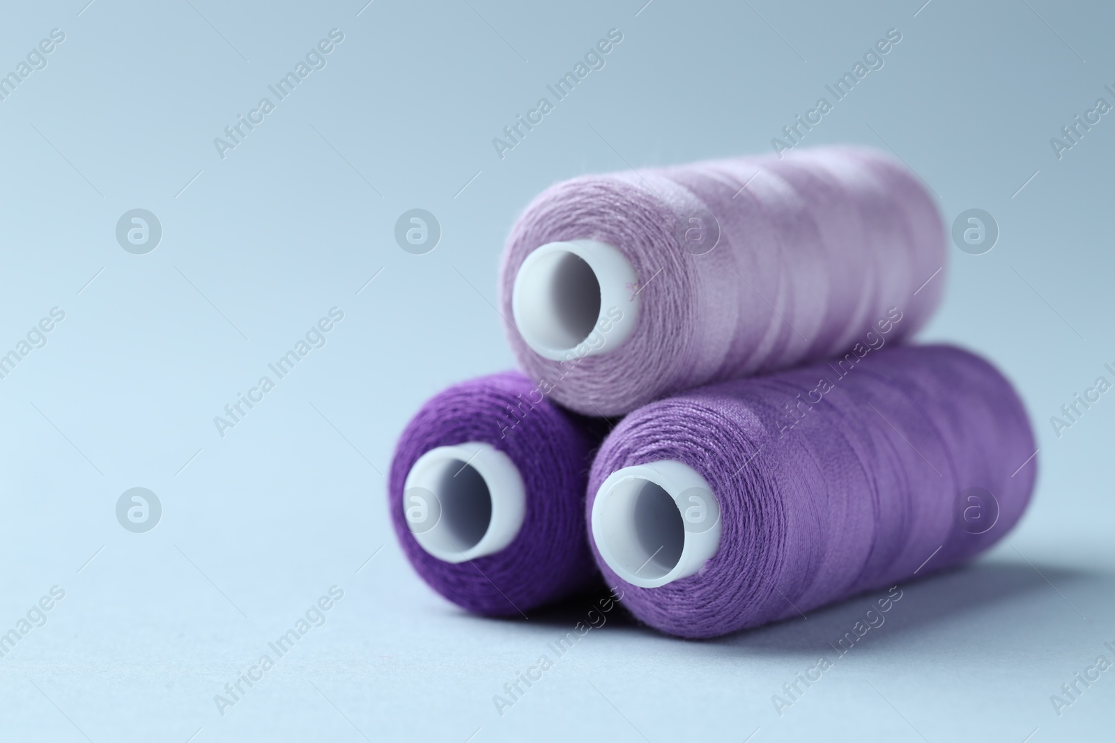 Photo of Spools of colorful sewing threads on light background, closeup. Space for text