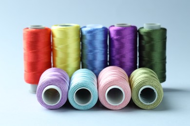 Photo of Spools of colorful sewing threads on light background, closeup