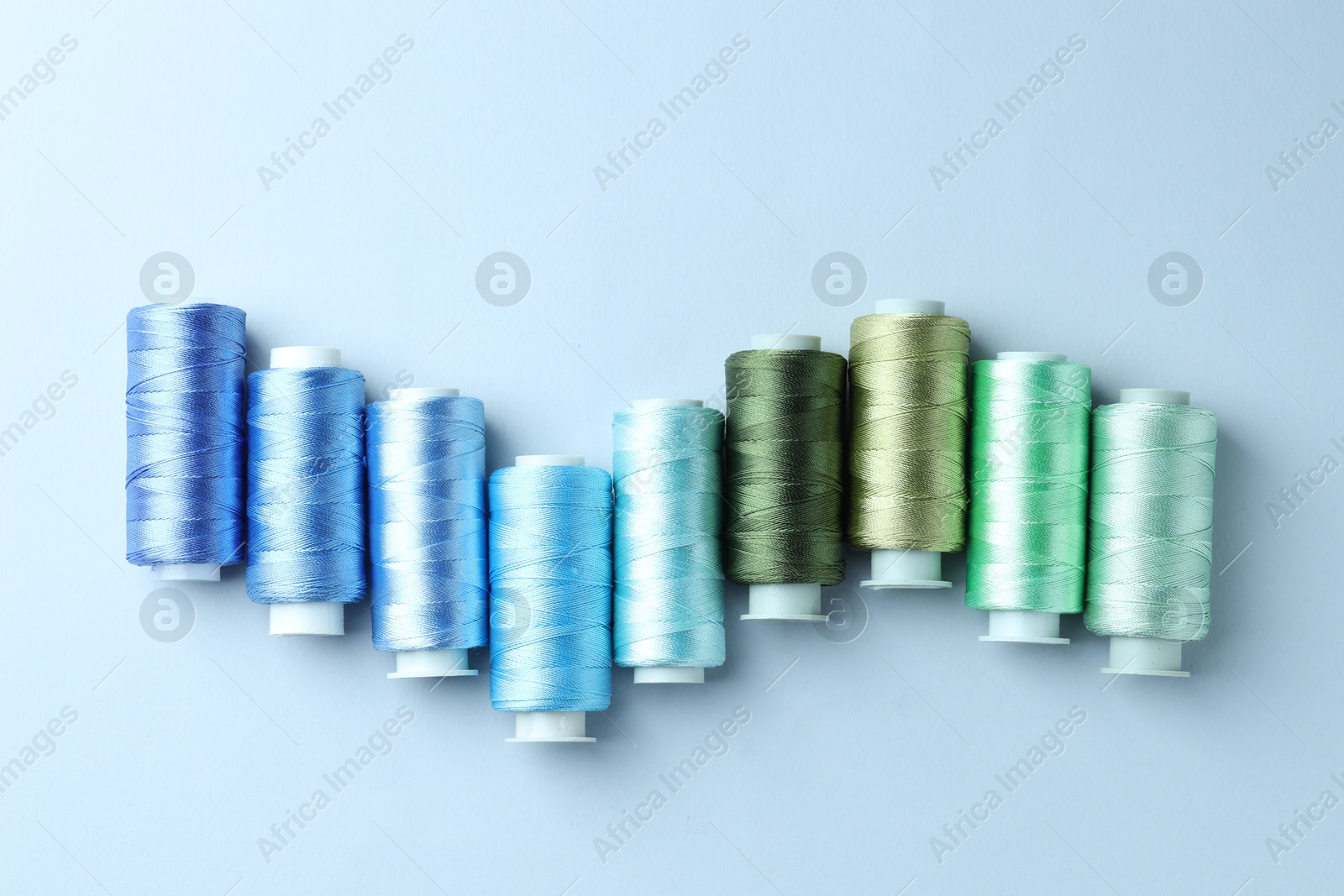 Photo of Spools of colorful sewing threads on light background, flat lay