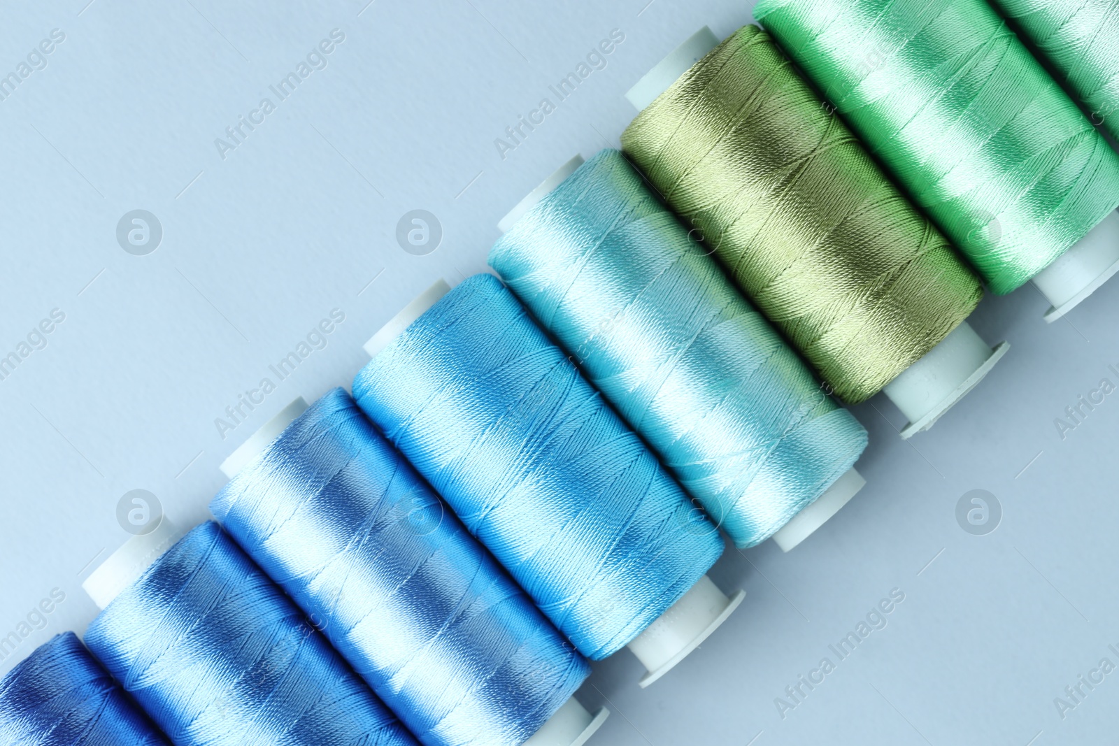 Photo of Spools of colorful sewing threads on light background, flat lay