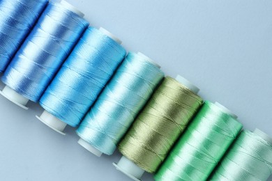 Photo of Spools of colorful sewing threads on light background, flat lay