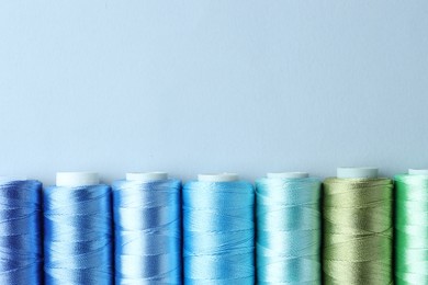 Photo of Spools of colorful sewing threads on light background, flat lay. Space for text