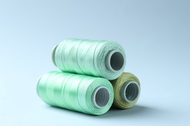 Photo of Spools of colorful sewing threads on light background, closeup