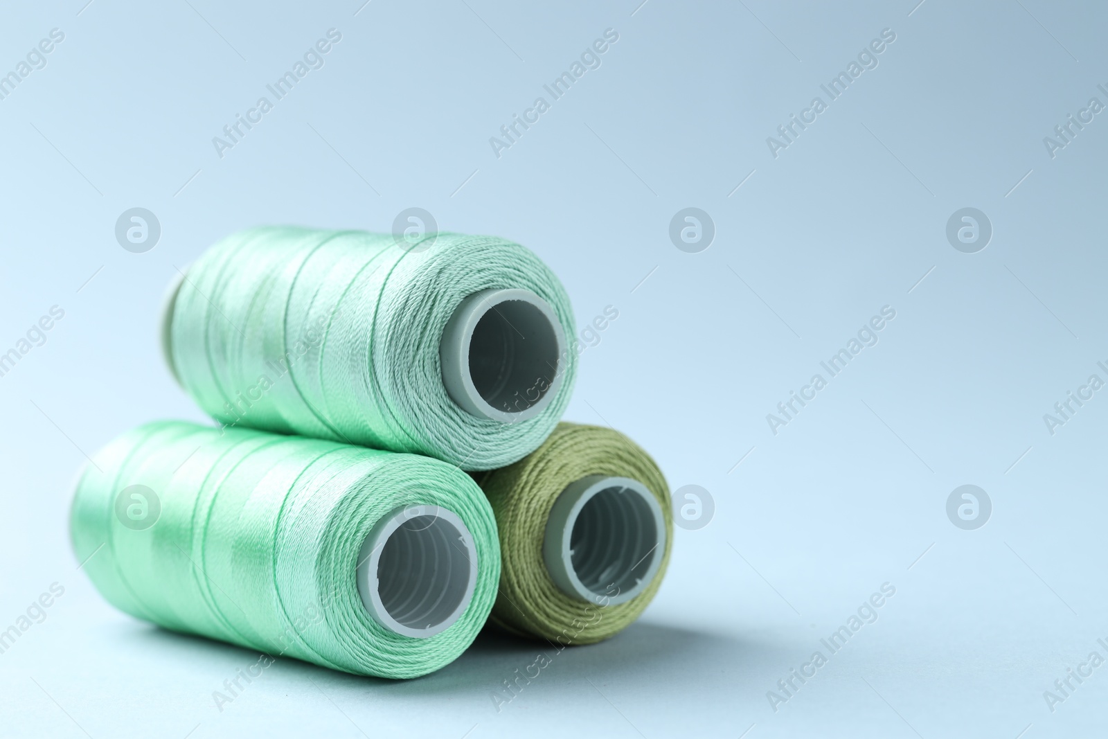 Photo of Spools of colorful sewing threads on light background, closeup. Space for text