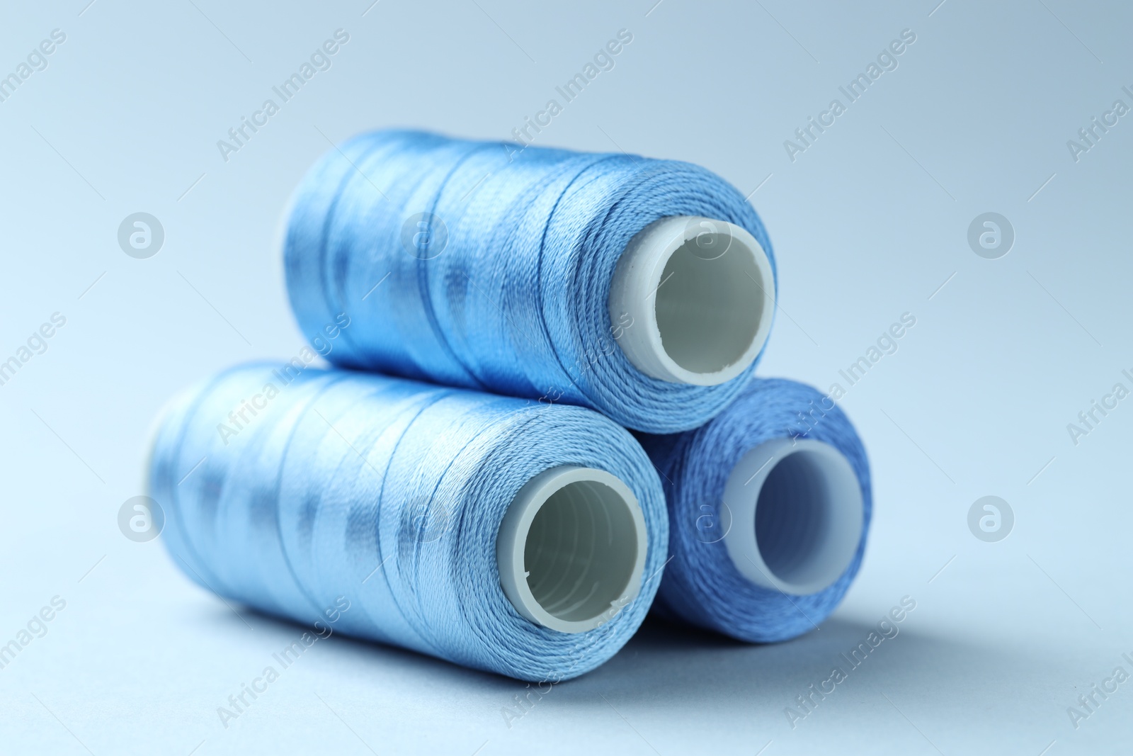 Photo of Spools of colorful sewing threads on light background, closeup