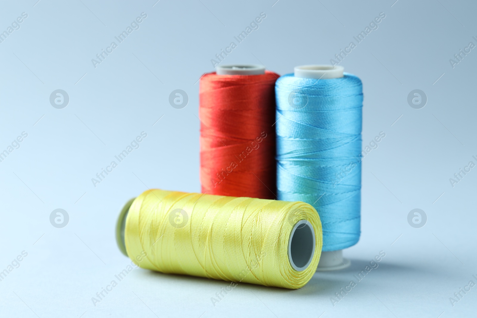 Photo of Spools of colorful sewing threads on light background, closeup