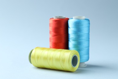 Photo of Spools of colorful sewing threads on light background, closeup