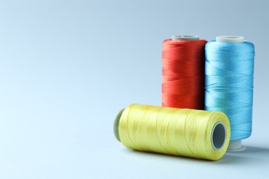 Photo of Spools of colorful sewing threads on light background, closeup. Space for text