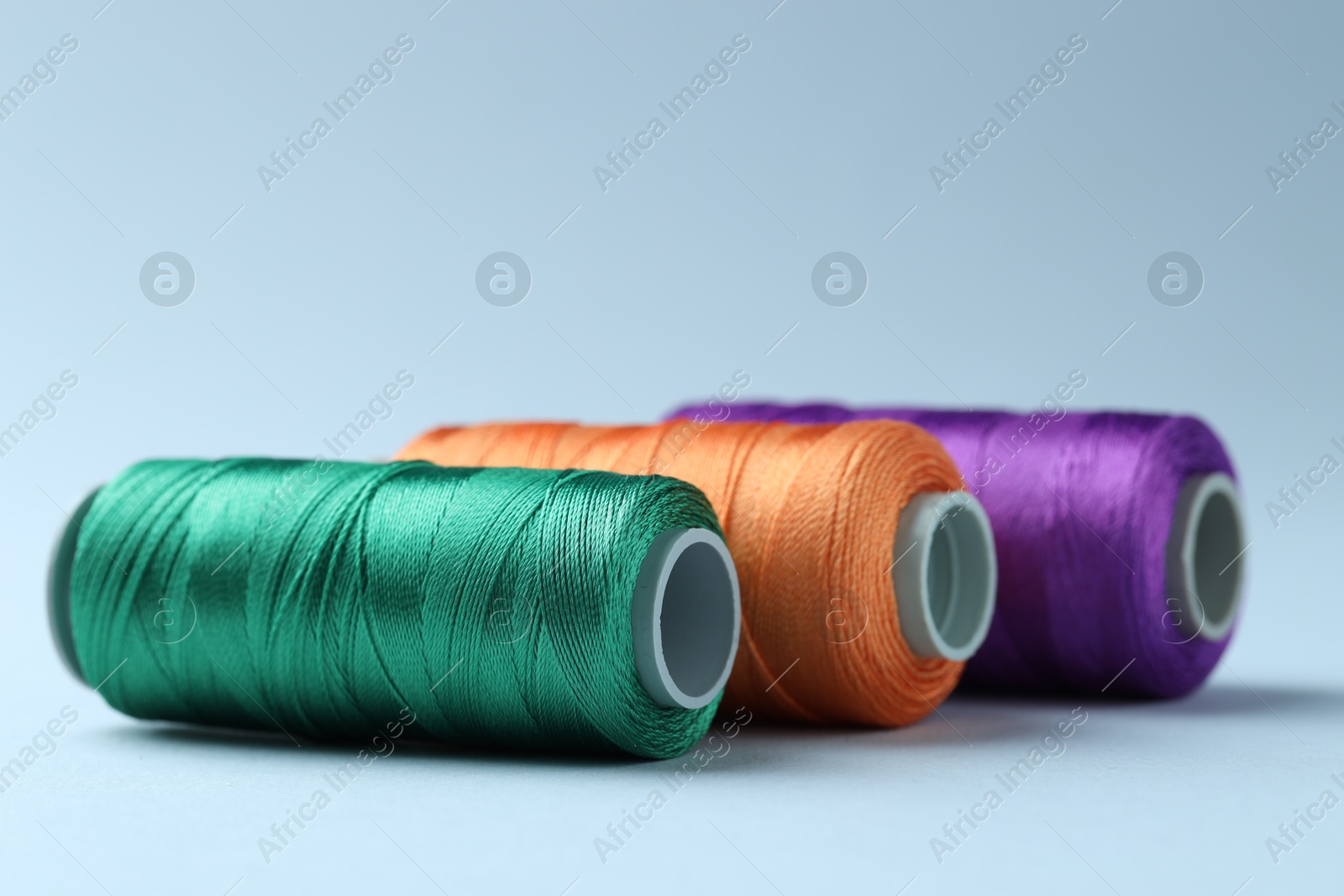 Photo of Spools of colorful sewing threads on light background, closeup