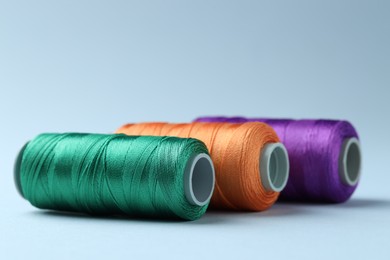 Photo of Spools of colorful sewing threads on light background, closeup