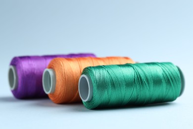 Photo of Spools of colorful sewing threads on light background, closeup