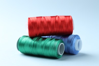 Photo of Spools of colorful sewing threads on light background, closeup