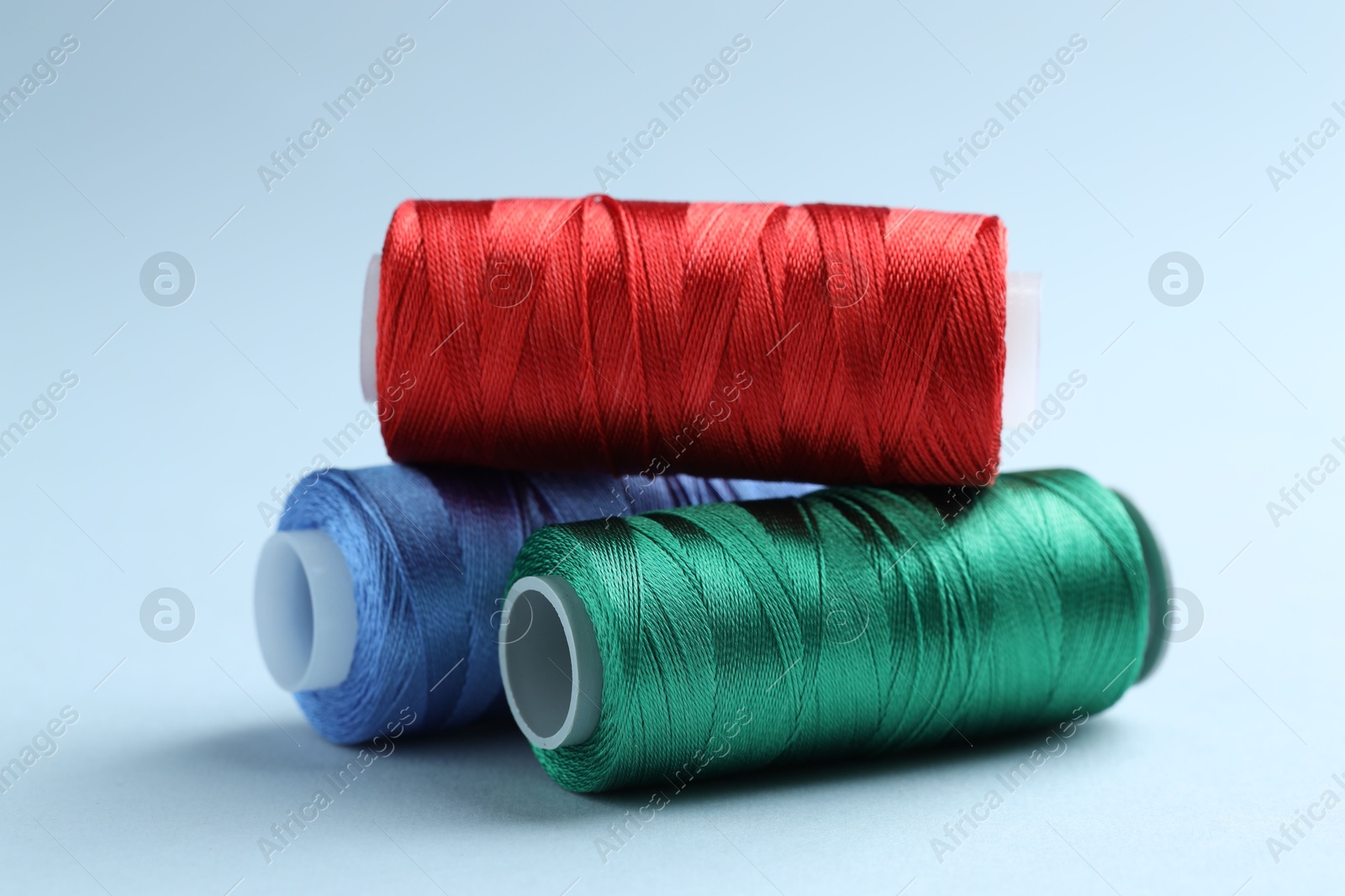 Photo of Spools of colorful sewing threads on light background, closeup