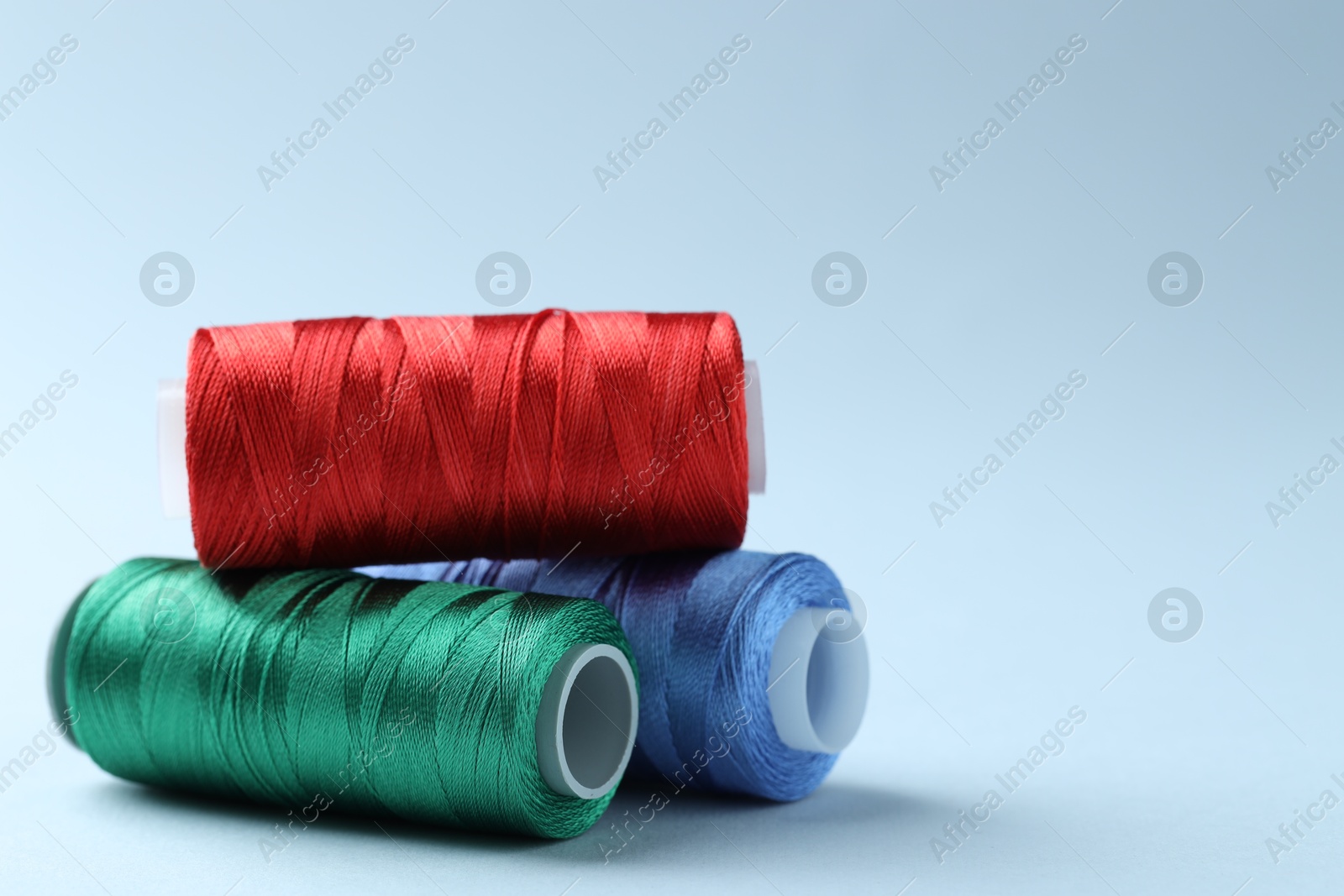 Photo of Spools of colorful sewing threads on light background, closeup. Space for text