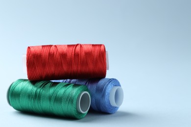 Photo of Spools of colorful sewing threads on light background, closeup. Space for text