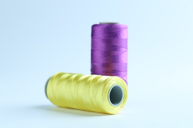 Photo of Spools of colorful sewing threads on light background, closeup