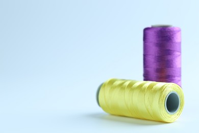 Photo of Spools of colorful sewing threads on light background, closeup. Space for text