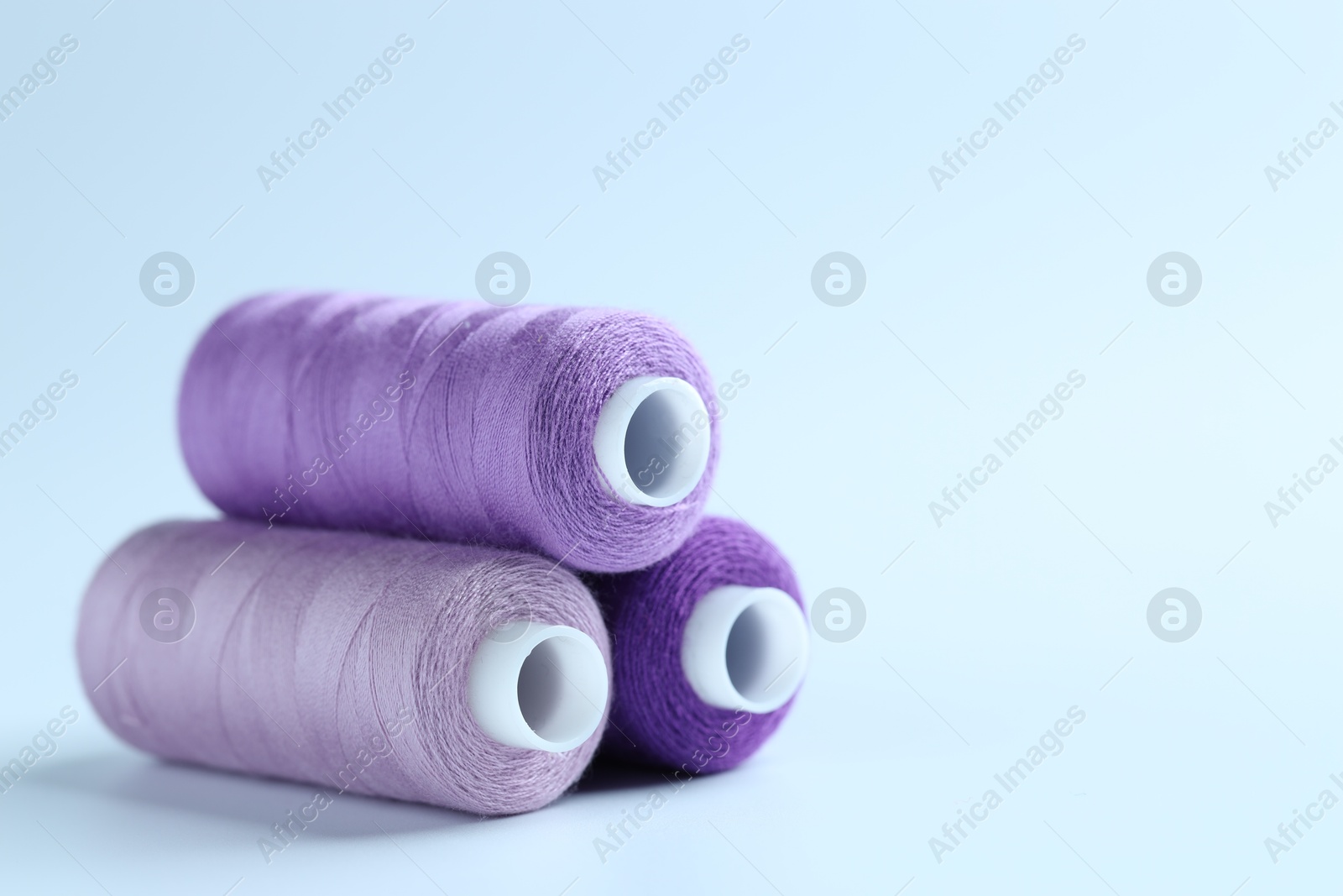 Photo of Spools of colorful sewing threads on light background, closeup. Space for text