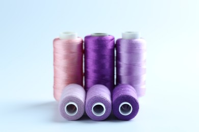 Photo of Spools of colorful sewing threads on light background, closeup