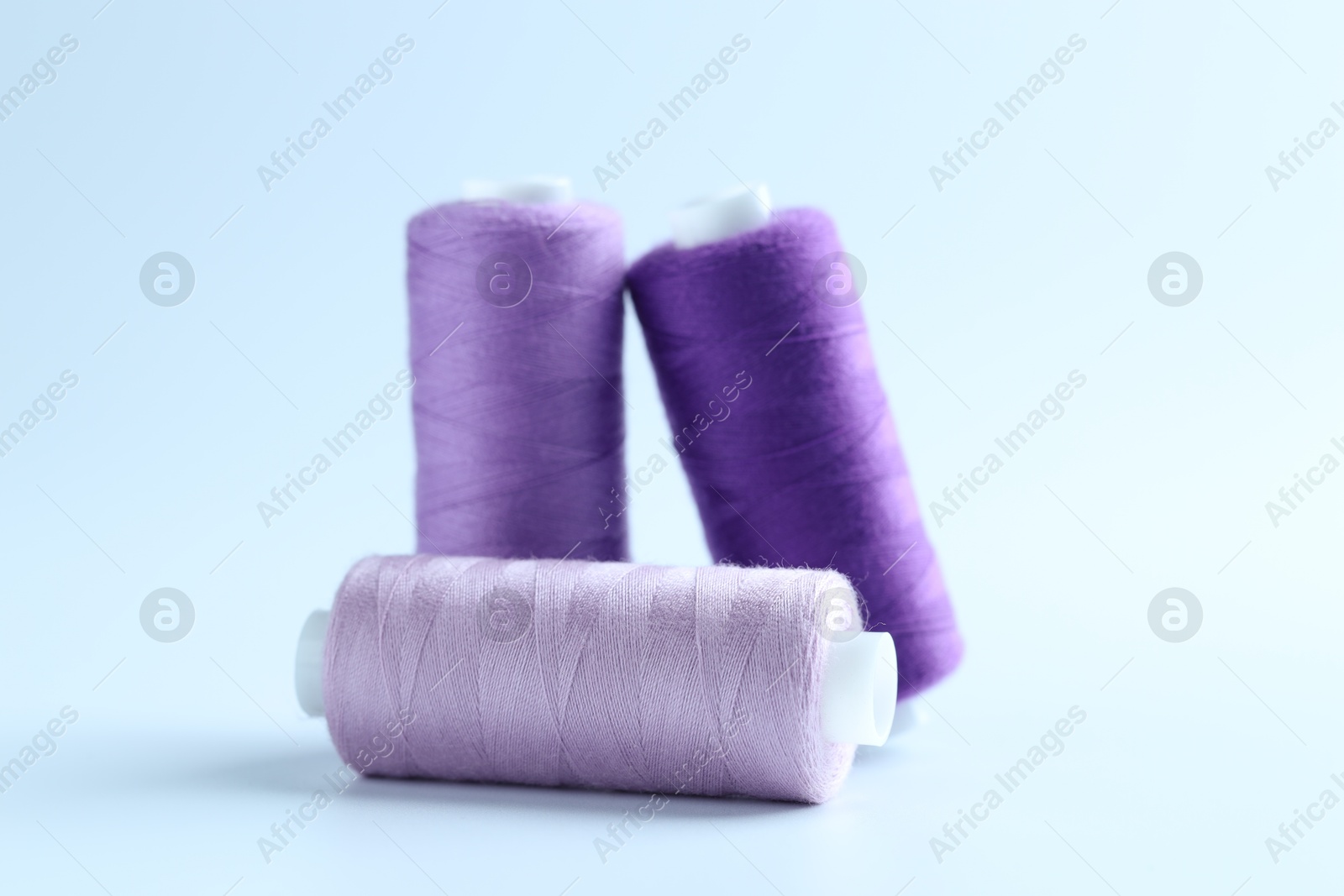 Photo of Spools of colorful sewing threads on light background, closeup