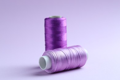 Photo of Spools of colorful sewing threads on lilac background, closeup