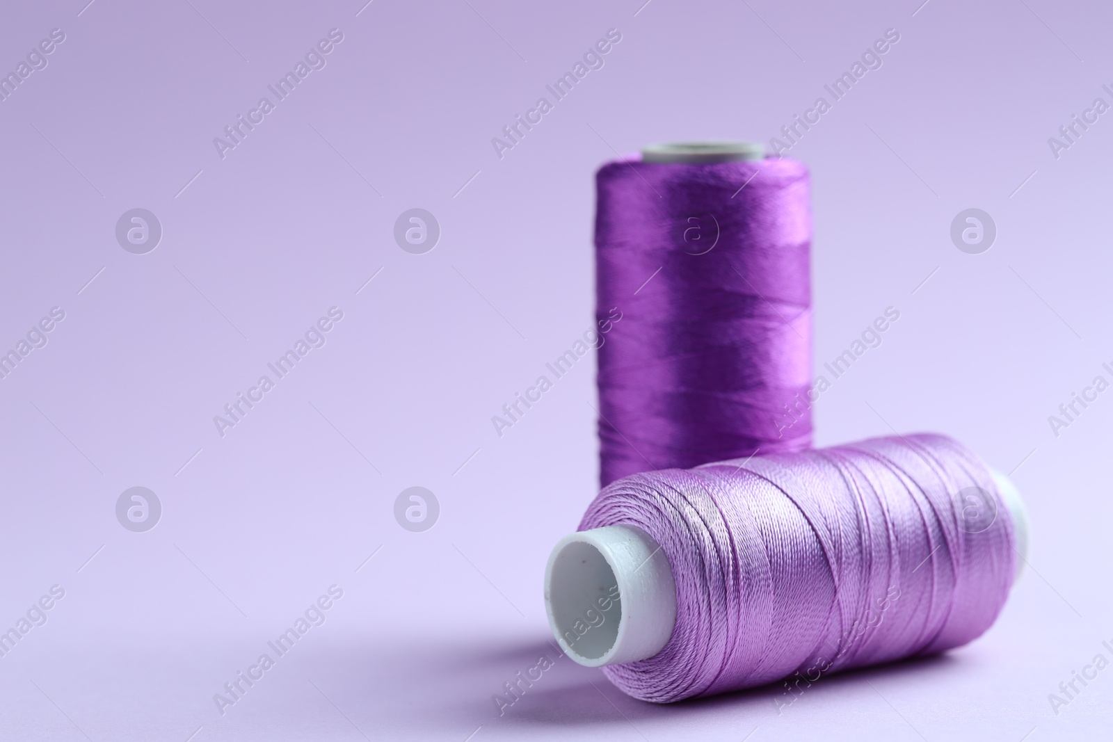 Photo of Spools of colorful sewing threads on lilac background, closeup. Space for text